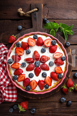 Delicious strawberry pie with fresh blueberry and whipped cream on wooden rustic table, cheesecake, top view