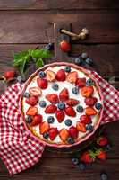 Delicious strawberry pie with fresh blueberry and whipped cream on wooden rustic table, cheesecake, top view