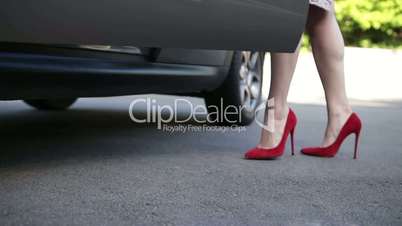 Elegant female legs in red heels getting into car