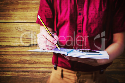 Composite image of mid section of student with mobile phone writing on notebook