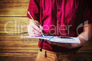 Composite image of mid section of student with mobile phone writing on notebook