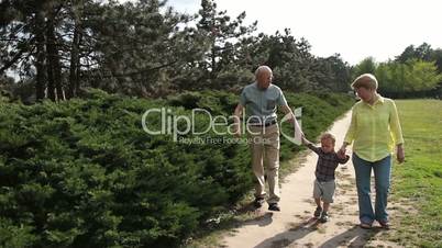 Toddler boy walking with his grandparents in park