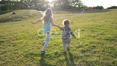 Joyful siblings running through green grassy field
