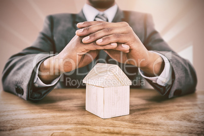 Composite image of businessman protecting house model with hands