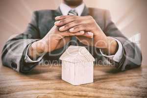Composite image of businessman protecting house model with hands