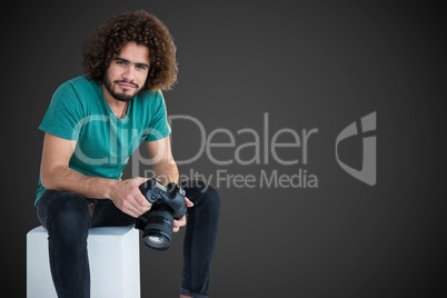 Composite image of portrait of male photographer holding camera while sitting on seat