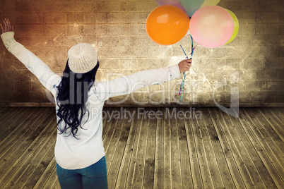 Composite image of full length rear view of carefree woman holding colorful balloons