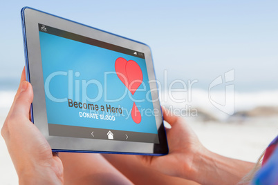 Composite image of woman sitting on beach in deck chair using tablet pc