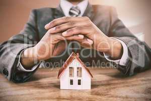 Composite image of businessman protecting house model with hands on table