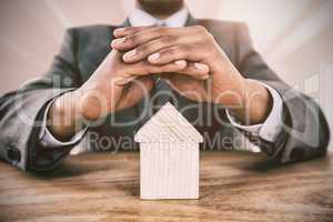 Composite image of businessman protecting house model with hands