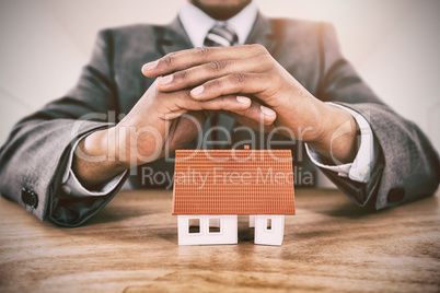 Composite image of businessman protecting house model with hands