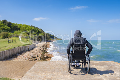 Disabled young man sitting in a wheelchair and looks at the sea