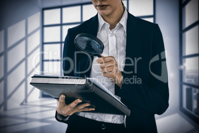 Composite image of businesswoman looking at document through magnifying glass