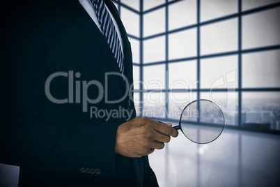 Composite image of mid section of businessman holding magnifying glass
