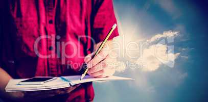 Composite image of mid section of student with mobile phone writing on notebook