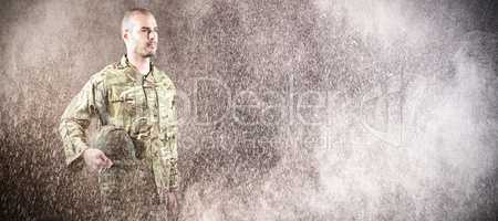 Composite image of confident soldier holding helmet while standing