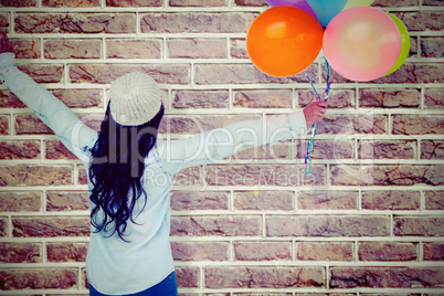 Composite image of full length rear view of carefree woman holding colorful balloons