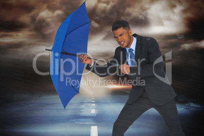Composite image of portrait of businessman defending with blue umbrella