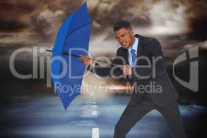 Composite image of portrait of businessman defending with blue umbrella