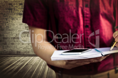 Composite image of mid section of student with mobile phone writing on notebook