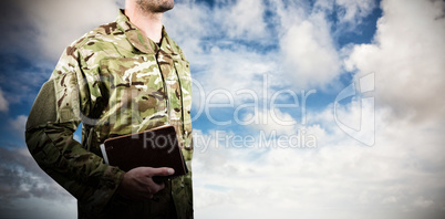 Composite image of mid section of soldier holding books while standing