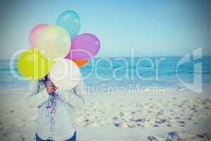 Composite image of woman hiding her face with bunch of colorful balloons