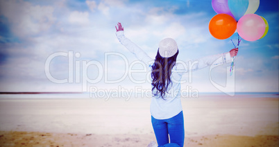 Composite image of full length rear view of carefree woman holding colorful balloons