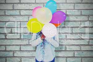 Composite image of woman hiding her face with bunch of colorful balloons