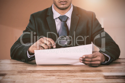 Composite image of businessman looking at document through magnifying glass