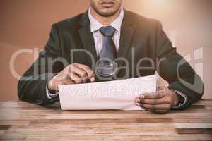 Composite image of businessman looking at document through magnifying glass