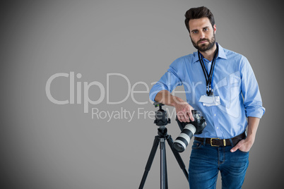 Composite image of portrait of serious young photographer holding camera while leaning on tripod