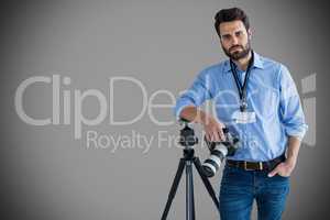 Composite image of portrait of serious young photographer holding camera while leaning on tripod