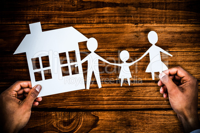 Composite image of hands holding a family with her house in paper