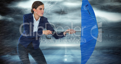 Composite image of confident businesswoman defending with blue umbrella
