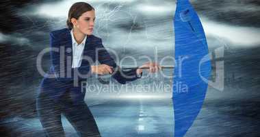 Composite image of confident businesswoman defending with blue umbrella