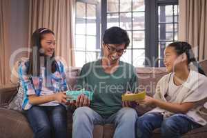 Father receiving greeting card and gift box from siblings in living room
