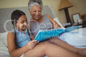 Grandmother and granddaughter watching photo album together in bed room