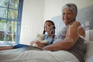 Grandmother and granddaughter holding photo album in bed room