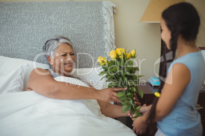 Granddaughter giving flowers to grandmother in bed room