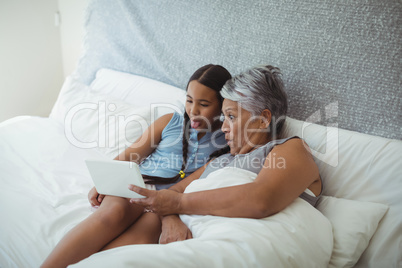 Grandmother and granddaughter using digital tablet in bed room