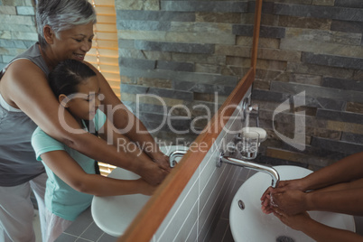 Grandmother and granddaughter washing hands in bathroom sink