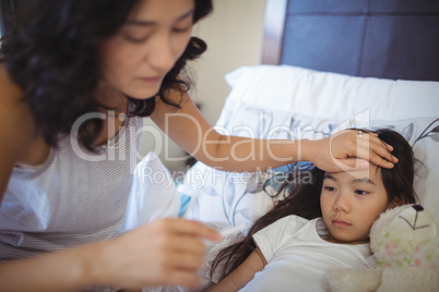 Mother checking body temperature of sick daughter in bed room