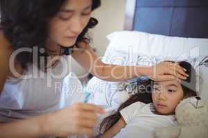 Mother checking body temperature of sick daughter in bed room