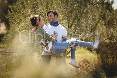 Young man carrying girlfriend by trees at farm