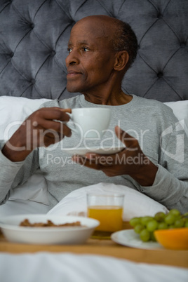 Thoughtful senior man looking away while having breakfast on bed