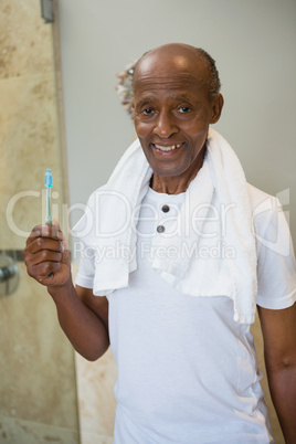 Portrait of smiling senior man holding toothbrush against wall