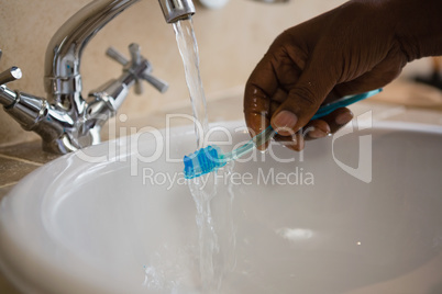 Cropped hand on man washing toothbrush in bathroom sink
