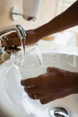 Cropped hands of man filling drinking glass at sink