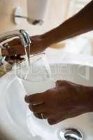 Cropped hands of man filling drinking glass at sink