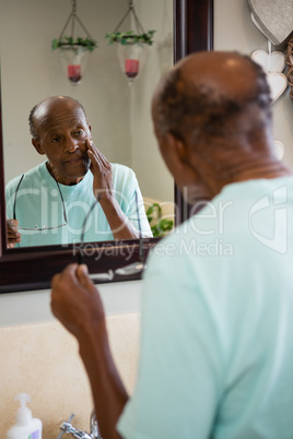 Concerned senior man touching cheek while looking into mirror